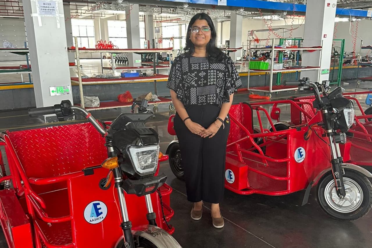 Aashita-badged red electric three-wheelers on the production floor, with a member of the team standing beside them